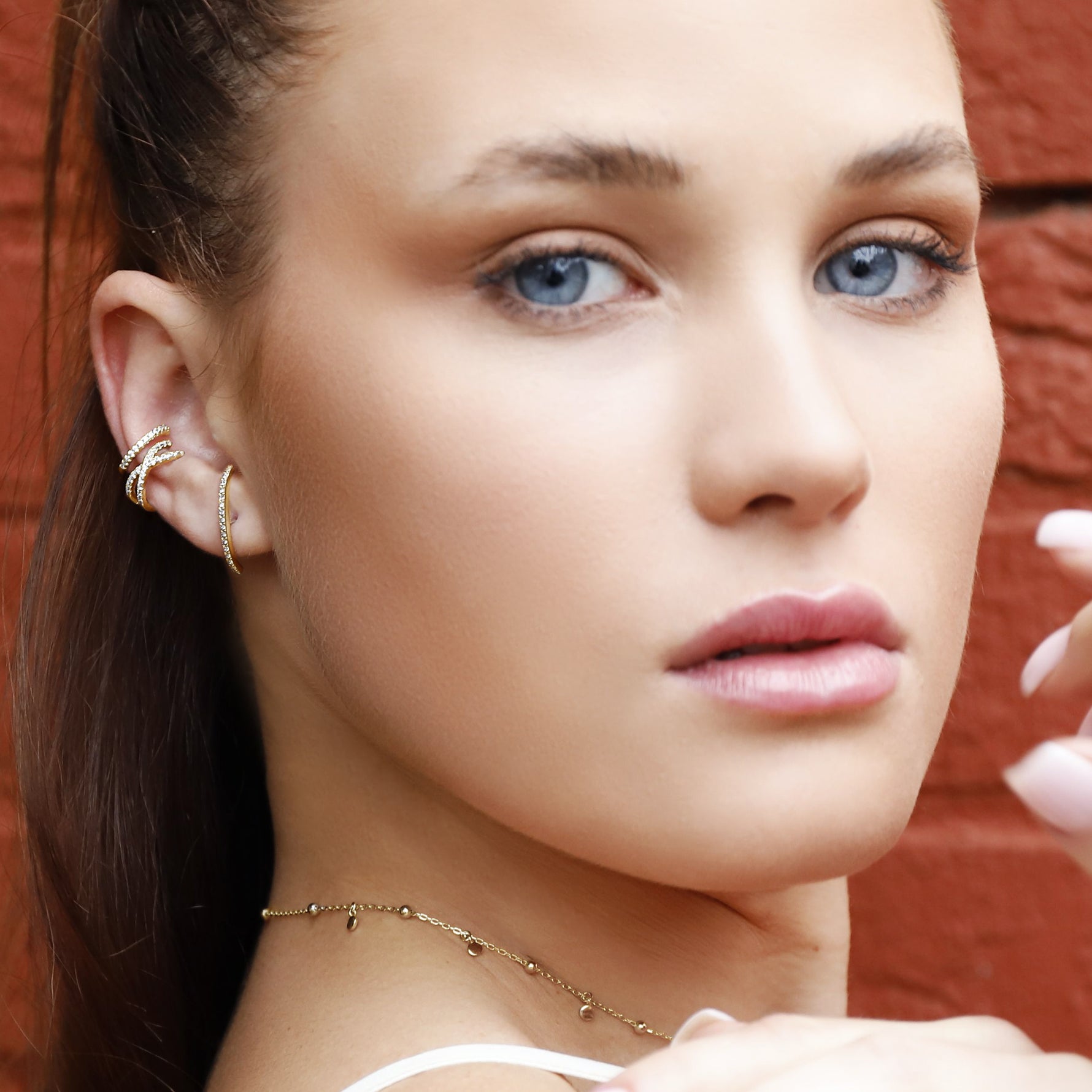 Close-up of AJJ Naomi gold ear cuff featuring a dainty curved bar design with cz embellishments on the conch and huggie style.