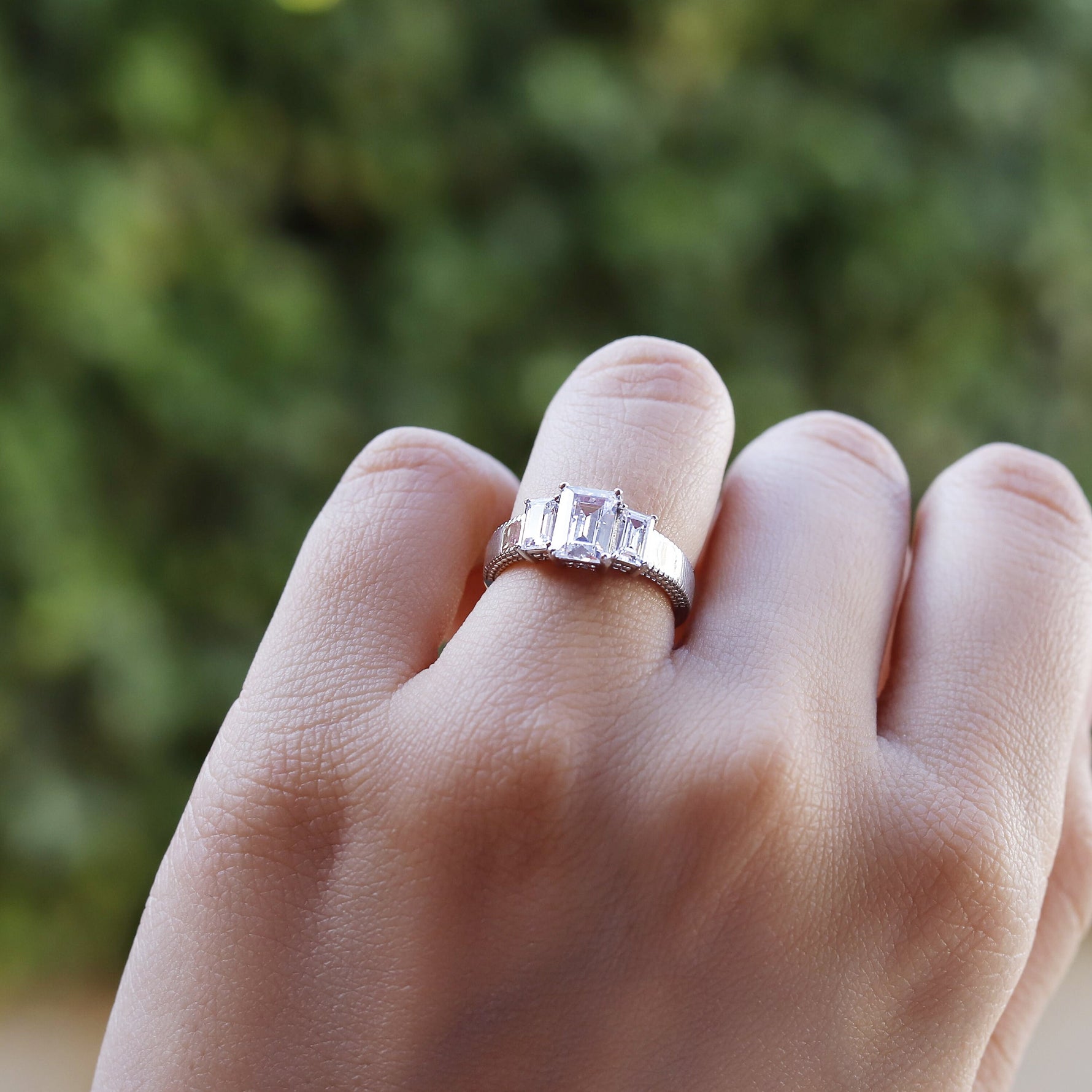 AJJ sterling silver engagement ring featuring a 2.5 ct emerald trilogy design, ideal as a promise or bridal ring.
